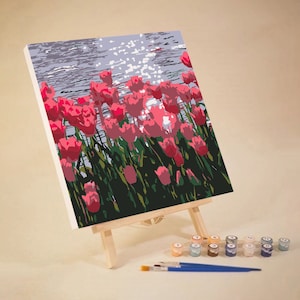 May include: A paint by numbers canvas featuring a close-up of pink tulips in a field. The canvas is on an easel with paint pots and brushes.