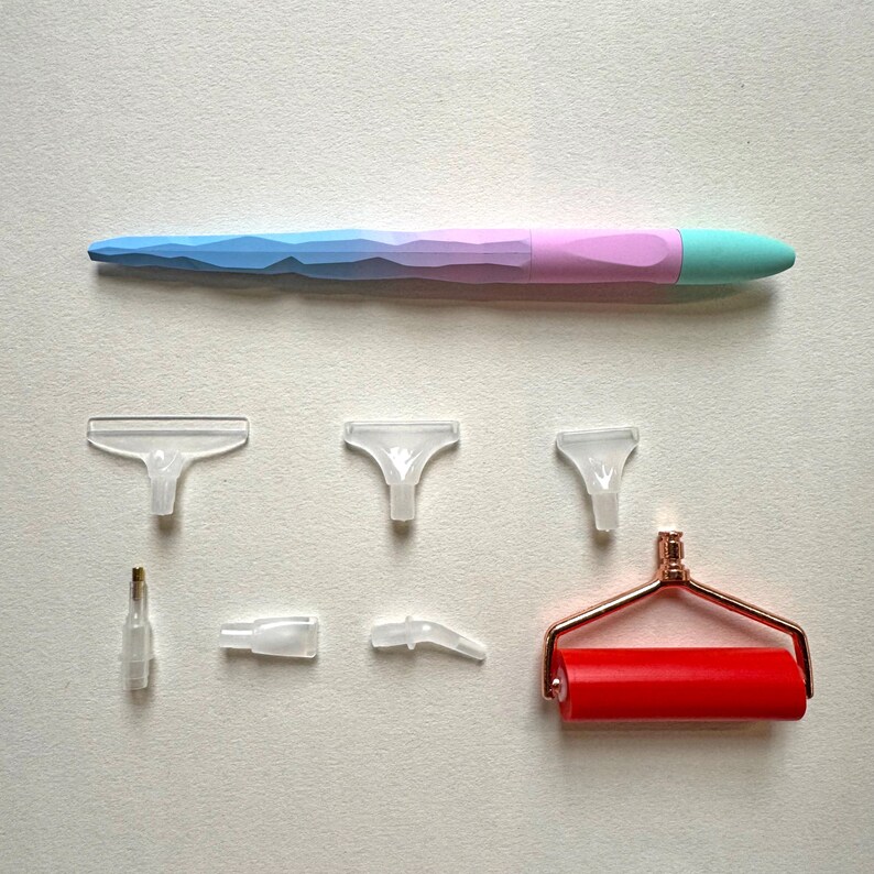 May include: A diamond painting kit with a multi-colored pen, clear plastic applicator tips, a small glue bottle, and a red roller with a rose gold handle. The pen is blue, pink, and green. The kit is for crafting and art projects.