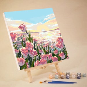 May include: A paint by numbers canvas depicting a sunset over a body of water with pink tulips in the foreground. The canvas is on an easel and there are paint pots with numbers on them.