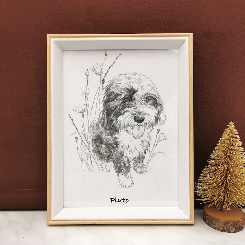 May include: A framed pencil sketch of a dog with a white and black coat, tongue out, surrounded by flowers. The dog's name, "Pluto," is written below the image. The frame is light wood.