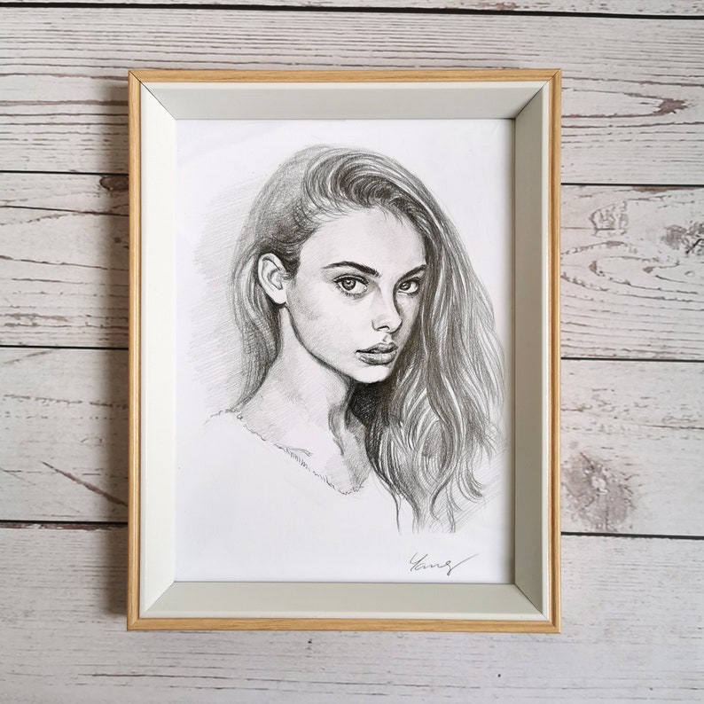 May include: A framed black and white pencil drawing of a woman with long hair looking directly at the viewer. The drawing is signed "King" in the bottom right corner.