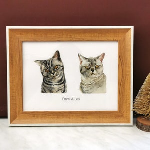 May include: A framed watercolor painting of two cats, Emmi and Leo, with a brown wooden frame and a white mat.