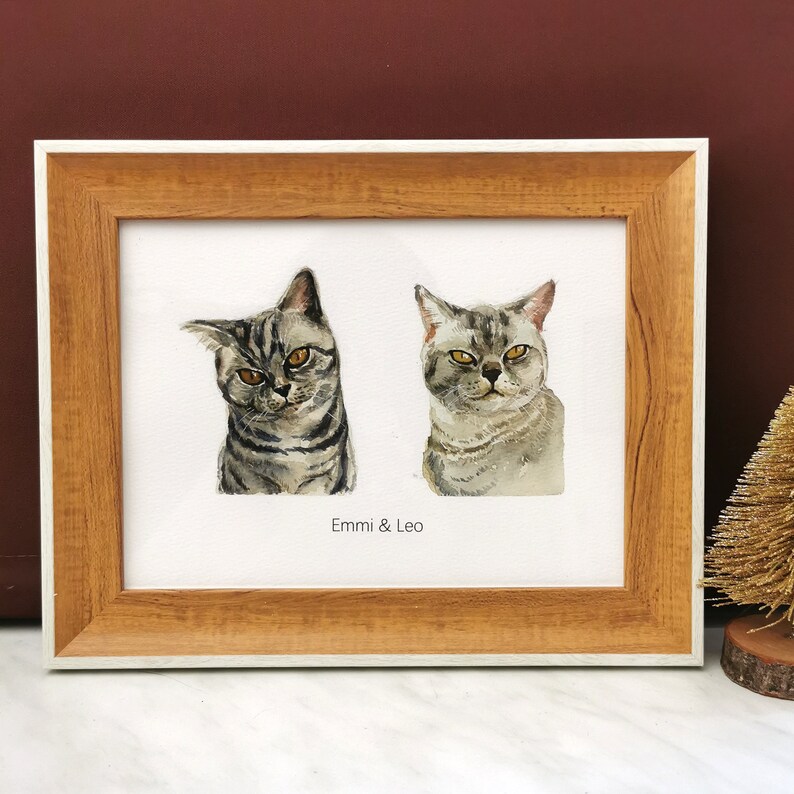 May include: A framed watercolor painting of two cats, Emmi and Leo, with a brown wooden frame and a white mat.
