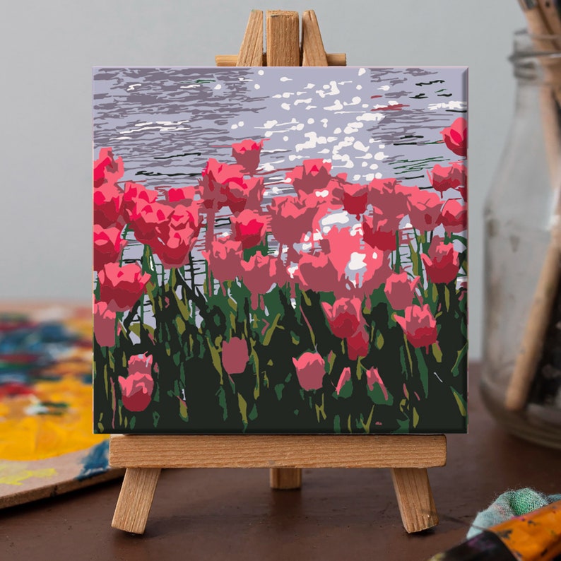 May include: A painting on canvas depicting a field of pink tulips with a blue water background. The painting is displayed on a small wooden easel.