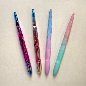 May include: Four colorful pens with faceted, jewel-like barrels. The pens transition from blue to purple, red to gold, blue to pink, and pink to green. The pens are arranged diagonally against a white background.
