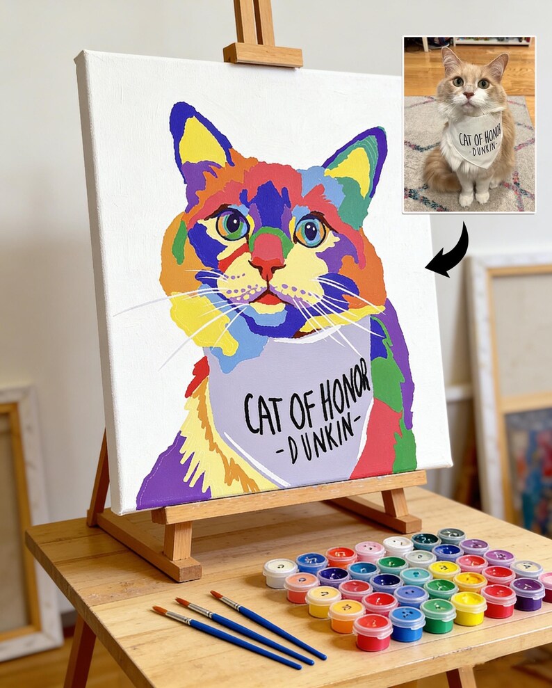 May include: A colorful cat portrait on canvas, displayed on a wooden easel. The artwork features a vibrant, multi-colored cat with the text "CAT OF HONOR - DUNKIN" on a bib. Paint pots and brushes are arranged below.