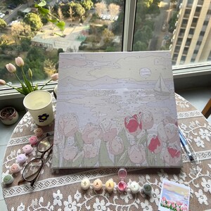 May include: A paint by numbers canvas showing a seascape with a sailboat in the distance and a field of pink tulips in the foreground. The canvas is on a table with paint pots and brushes.