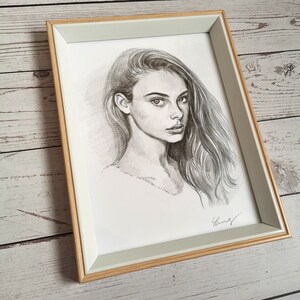 May include: A framed black and white pencil drawing of a woman with long hair. The woman is looking to the right of the frame. The drawing is signed in the bottom right corner.