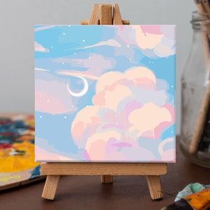 May include: A small canvas painting on an easel depicting a pastel pink and blue sky with white clouds and a crescent moon. The sky is dotted with white stars.
