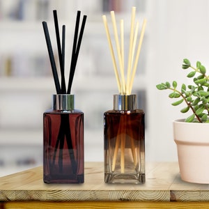 May include: Two glass diffuser bottles with different coloured liquids and sticks. The bottle on the left has black sticks and a dark brown liquid. The bottle on the right has natural coloured sticks and a light brown liquid. Both bottles have silver caps.