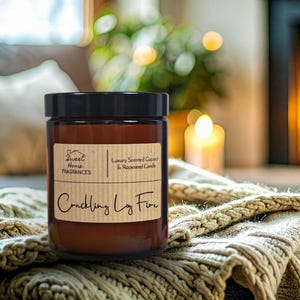 May include: A brown glass jar candle with a black lid. The label reads "Sweet Home Fragrances" and "Crackling Log Fire". The candle is on a knitted blanket, with a fireplace and soft lighting in the background. The candle is scented with coconut and rapeseed.