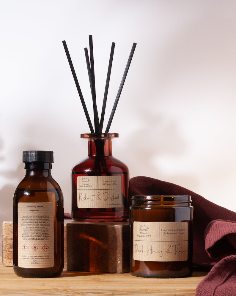May include: A reed diffuser in a dark amber glass bottle with black reeds, a dark amber glass candle jar labeled Dark Honey & Tobacco, and a dark amber glass refill bottle labeled Bewitching Berries, all featuring Sweet Home Fragrances labels.