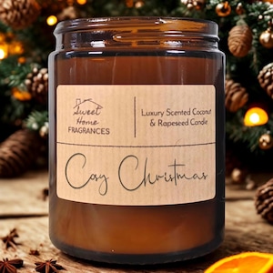 May include: A brown glass jar candle with a label that reads "Sweet Home Fragrances" and "Cozy Christmas." The candle is scented with coconut and rapeseed. The background includes Christmas decorations and a wooden surface.