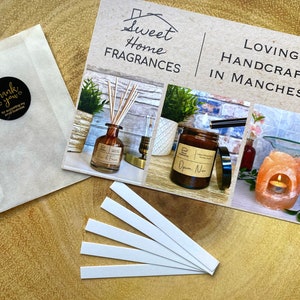May include: A set of six white fragrance testing strips, a brown paper envelope with a gold "Thank You" sticker, and a printed card with the text "Sweet Home Fragrances" and "Lovingly Handcrafted in Manchester". The card features three images of home fragrance products: a diffuser bottle, a candle, and a salt lamp.