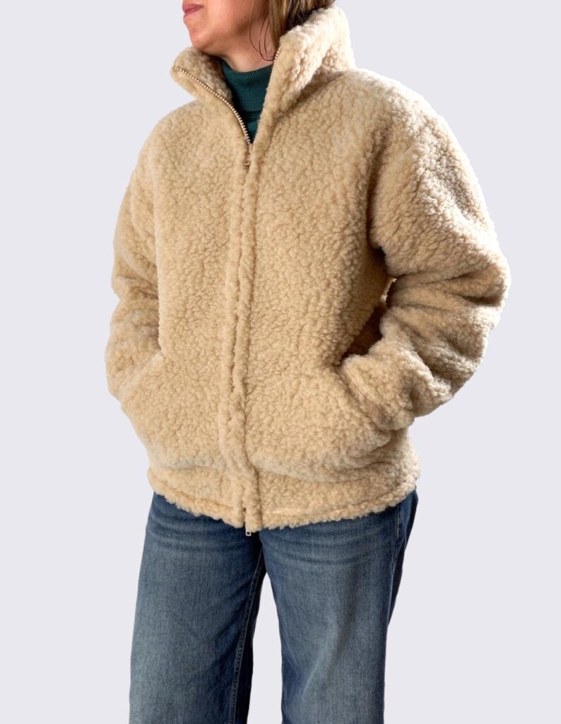 Oatmeal beige unisex merino wool jacket with full zip and high collar, displayed on model against neutral beige background.