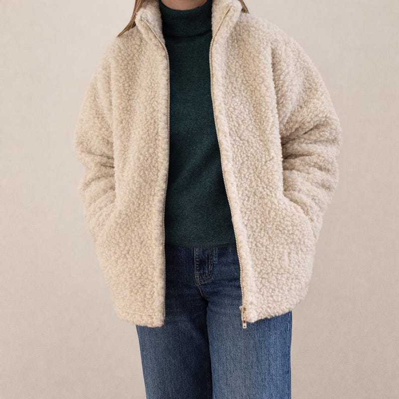 Oatmeal beige unisex merino wool jacket with full zip and high collar, displayed on model against neutral beige background.