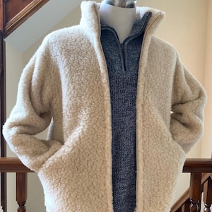 Oatmeal beige unisex wool jacket displayed on a mannequin, featuring a soft textured fabric, full zip front, high collar, and side pockets in an indoor setting
