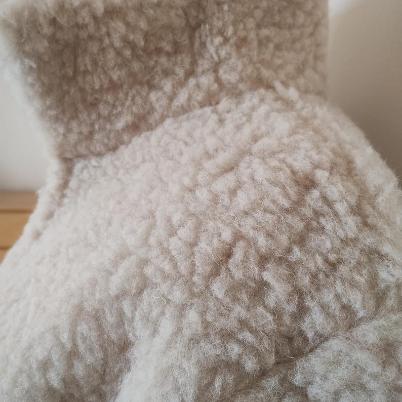 Close-up view of soft oatmeal merino wool fabric texture and knit detail on a natural neutral background.