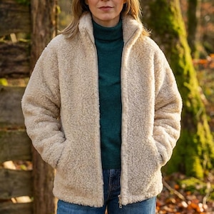 Female model wearing oatmeal merino wool jacket outdoors showing styling and fit on woodland background