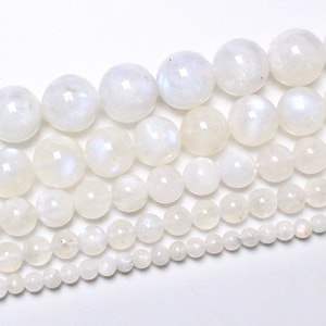 Può includere: Una collana di perle di pietra di luna bianca di diverse dimensioni. Le perle sono rotonde e lisce, con un sottile bagliore iridescente.