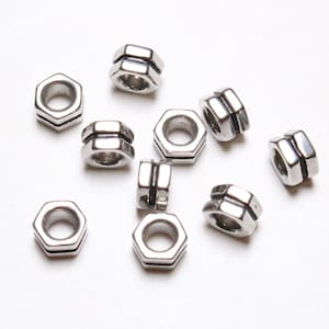 May include: Ten silver metal beads in the shape of a hexagon with a hole in the center. The beads are stacked on top of each other.