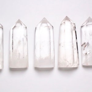 Puede incluir: Cinco puntas de cristal de cuarzo transparente dispuestas en fila sobre un fondo blanco.