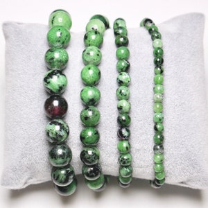 Peut inclure: Quatre bracelets en pierres précieuses vertes avec des taches noires et blanches. Les bracelets sont faits de perles rondes et sont présentés sur un coussin de velours gris.