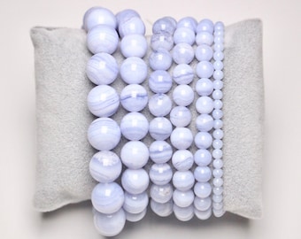 May include: A set of seven blue agate bead bracelets of varying sizes, stacked on a gray velvet cushion.