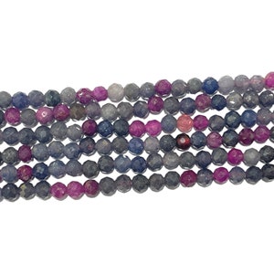 Può includere: Una collana di perline di pietre preziose sfaccettate in tonalità di blu, viola e rosa. Le perline sono rotonde e hanno una forma leggermente irregolare.