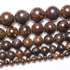 Peut inclure: Un brin de perles de pierres précieuses brunes et dorées. Les perles sont rondes et ont une finition lisse et polie. Les perles sont disposées en taille graduée, les plus grandes en haut et les plus petites en bas.