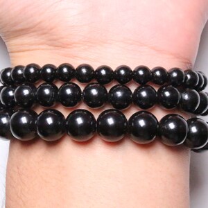 May include: Three black beaded bracelets stacked on a wrist. The beads are round and smooth, and the bracelets are made of natural stone.