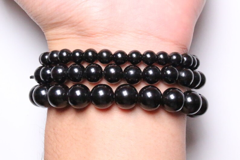 May include: Three black beaded bracelets stacked on a wrist. The beads are round and smooth, and the bracelets are made of natural stone.
