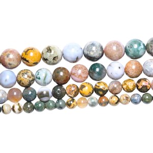 Puede incluir: Una hebra de cuentas redondas de piedra natural multicolores. Las cuentas son una mezcla de verde, marrón, amarillo y blanco con un patrón moteado.
