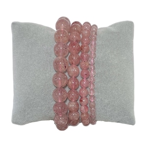 Peut inclure: Cinq bracelets en cristal rose avec des perles rondes, présentés sur un coussin en velours gris.