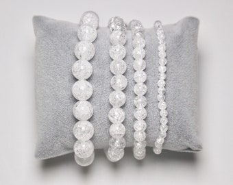 May include: Five white crystal bead bracelets stacked on a gray velvet cushion. The bracelets are made of clear, faceted beads.