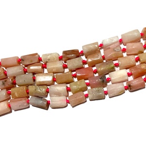 Peut inclure: Un brin de perles rectangulaires en pierres précieuses roses, brunes et blanches enfilées sur un cordon rouge. Les perles sont de tailles et de formes différentes et ont un aspect naturel et poli.