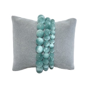 May include: Three turquoise blue beaded bracelets stacked on a gray velvet cushion.