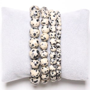 Puede incluir: Cinco pulseras apiladas hechas de cuentas de jaspe dalmata blanco y negro.