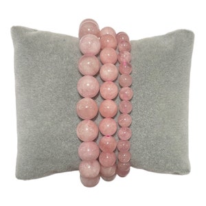 Peut inclure: Trois bracelets en quartz rose rose sur un coussin de velours gris. Les bracelets sont faits de perles rondes.