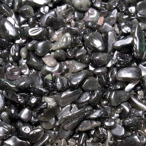 Puede incluir: Primer plano de un montón de piedras de obsidiana negra pulidas. Las piedras varían en tamaño y forma, con una superficie lisa y reflectante. La obsidiana es de un negro profundo y brillante, con algunas piedras que muestran toques de verde y gris.