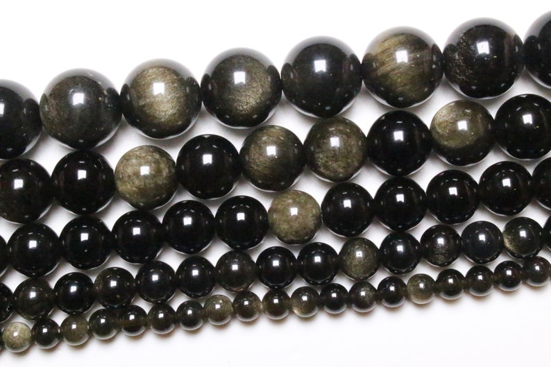 May include: A strand of black and gold gemstone beads. The beads are round and have a smooth, polished finish. The beads are arranged in a graduated size, with the largest beads at the top and the smallest beads at the bottom.