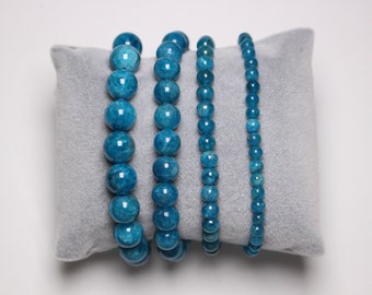 May include: Four blue gemstone bracelets with round beads on a gray velvet cushion. The bracelets are different lengths and have varying bead sizes.