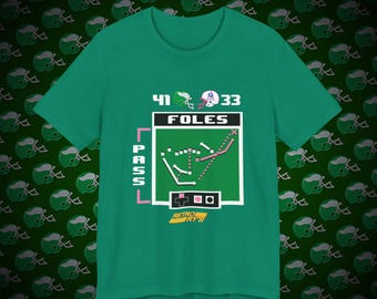 May include: A green t-shirt with a retro video game design featuring a football play with the text "41 Foles 33" and "PASS" on the side. The design also includes a retro video game controller and the text "Retro R'ys".