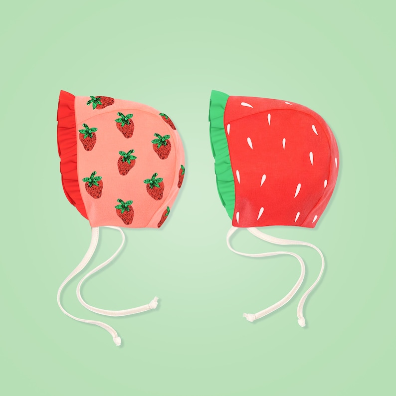 Peut inclure: Deux bonnets de b&eacute;b&eacute; avec des motifs de fraises. Un bonnet est rose avec des fraises rouges et l'autre est rouge avec des fraises vertes.