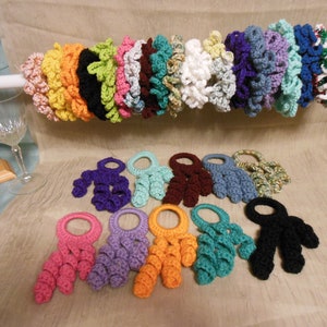 May include: A collection of colorful crocheted napkin rings. The rings are made with a variety of colors, including pink, purple, blue, green, orange, and black. The rings are all in the shape of a circle with a small loop at the top.