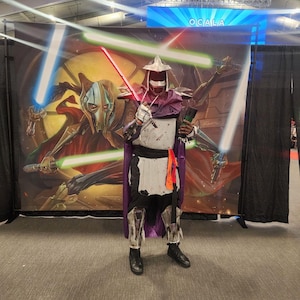 May include: A person dressed as a fictional character, wearing a purple and white costume with a mask, holding a lightsaber. The background is a large banner with a graphic of a character from a science fiction movie.