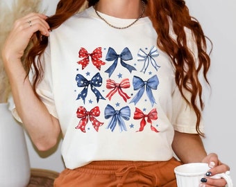 May include: A white t-shirt with a red, white, and blue bow pattern. The bows are arranged in a grid pattern and are surrounded by white stars.