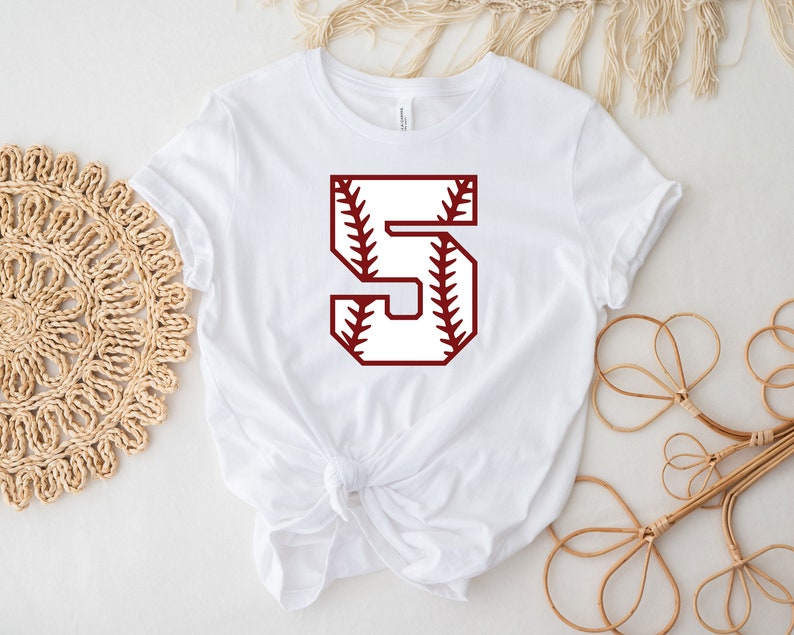 May include: White t-shirt with a red baseball-themed number 5 on the front.