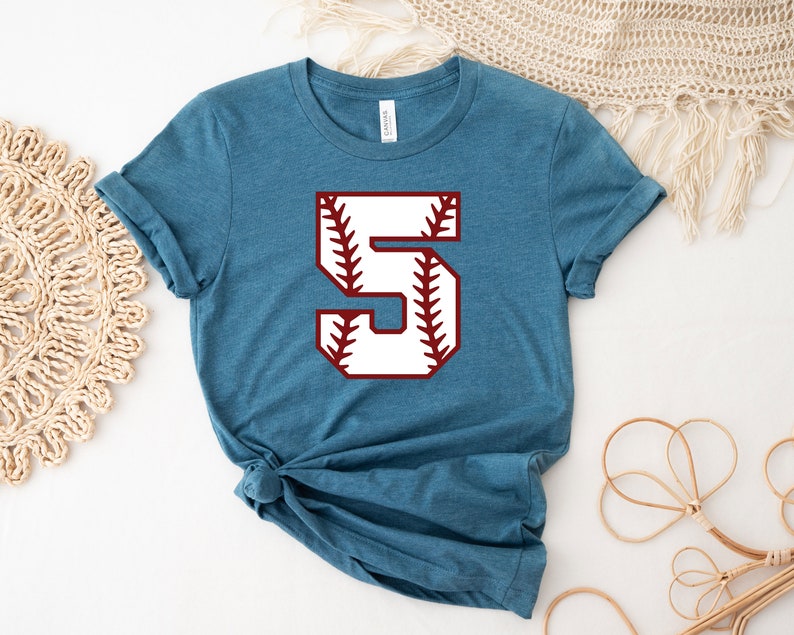 May include: A teal blue t-shirt with a white baseball number "5" with red stitching. The number is centered on the shirt.