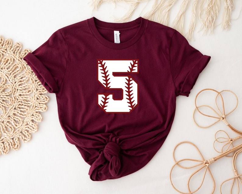 May include: Burgundy short-sleeved t-shirt with a white baseball-themed number "5" graphic.